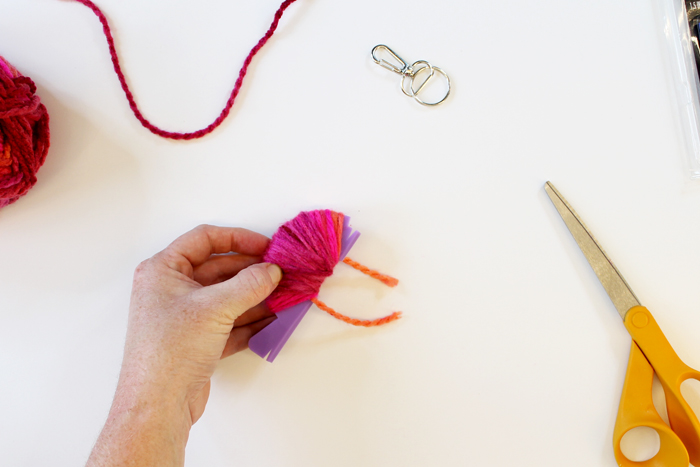 person wrapping pink yarn around small purple pom pom loom