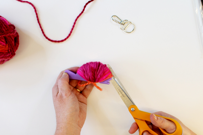 person wrapping pink yarn around small purple pom pom loom