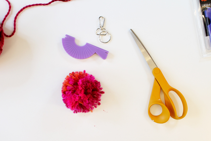 person wrapping pink yarn around small purple pom pom loom