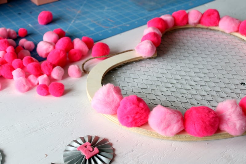 top shot of pink pompoms hot glued to wooden heart frame