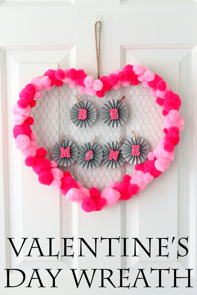 valentine's day wreath with "BE MINE" letters hanging on white door