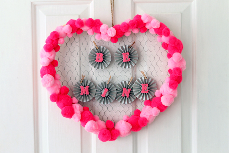 valentine's day wreath with "BE MINE" letters hanging on white door