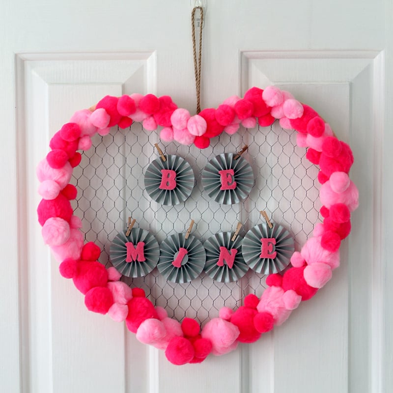 valentine's day wreath with "BE MINE" letters hanging on white door