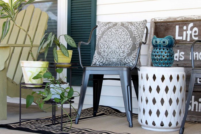 plants on a plant stand next to a metal chair on a porch