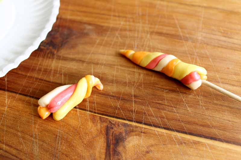 colored strands of candy wrapped together to create a horn, attached to a wooden skewer