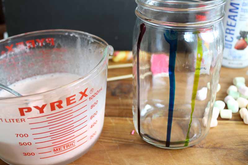 milkshake blended in glass pyrix measurer next to mason jar with food coloring dripped down the sides