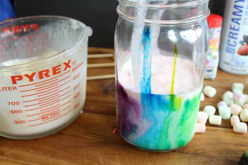 mason jar with food coloring dripped down the sides half filled with milkshake