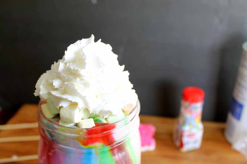 close up shot of colorful milkshake in mason jar topped with whipped cream