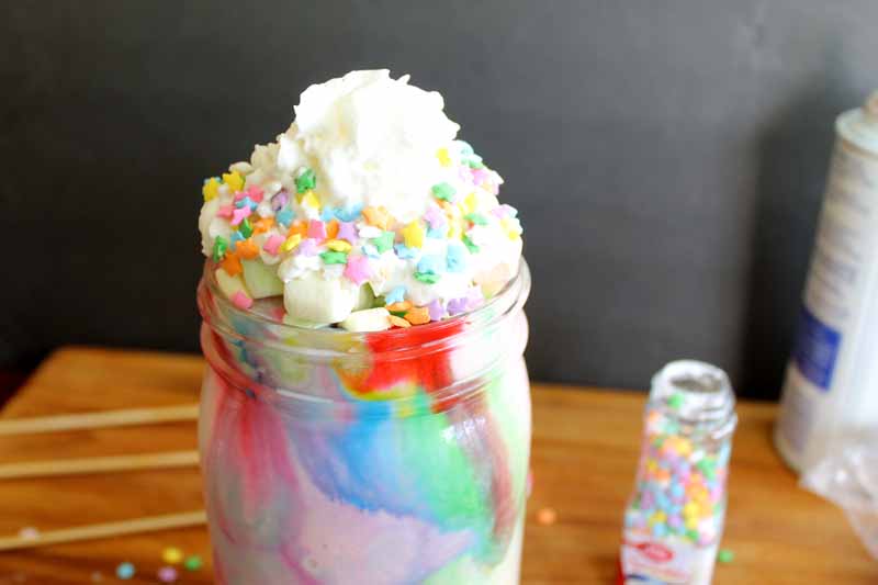 close up shot of colorful milkshake in mason jar topped with whipped cream and sprinkles