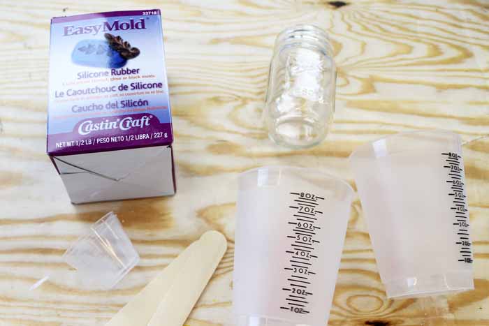 Supplies for creating a candle mold including measuring cups, mason jars and silicone rubber mix