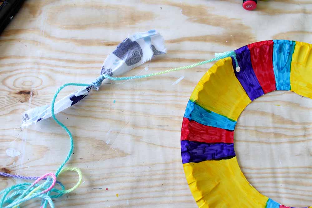 Attach yarn with fabric strips to the holes punched in your colorful paper plate kite