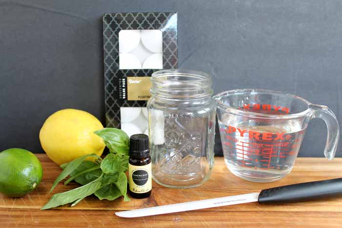 lemon, lime, basil, essential oils and candle making tools laid out on wooden table