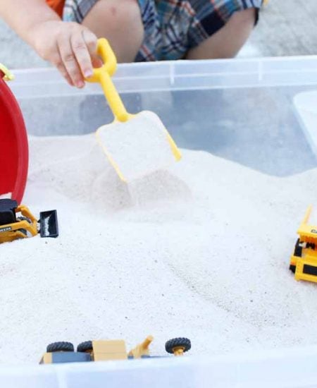 Front view of shovel scooping sand out of DIY sandbox