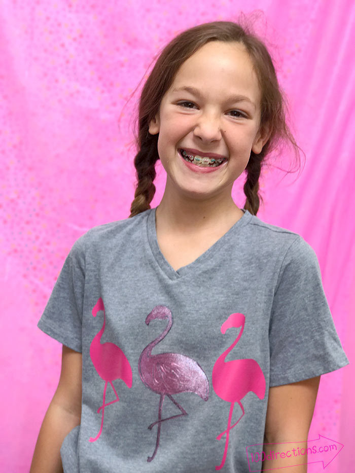 A girl wearing grey v neck with pink flamingos in front of pink