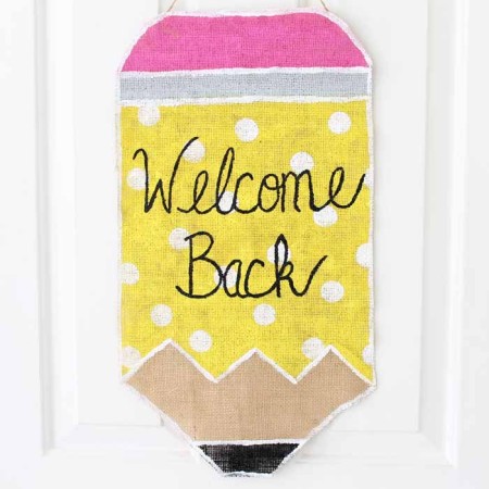 painted burlap pencil wall hanging on white door that says welcome back