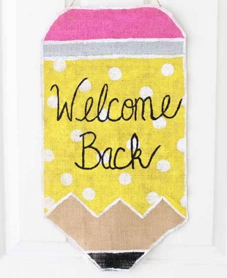 painted burlap pencil wall hanging on white door that says welcome back