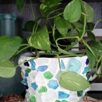 White planter decorated with blue sea glass and a plant overflowing from the pot.