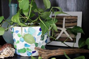 White planter decorated with blue sea glass and a plant overflowing from the pot.