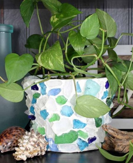 White planter decorated with blue sea glass and a plant overflowing from the pot.