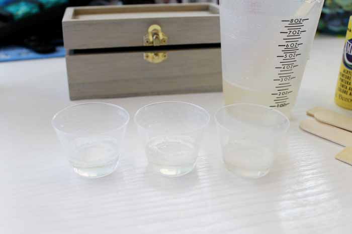 picture of three small plastic cups with plastic measuring cup and jewelry box on a white wooden backdrop