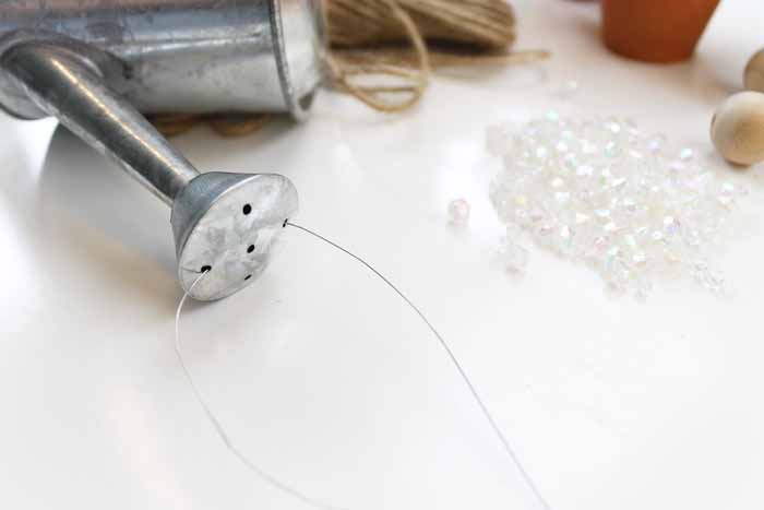 threading wire through watering can spout to make DIY wind chimes