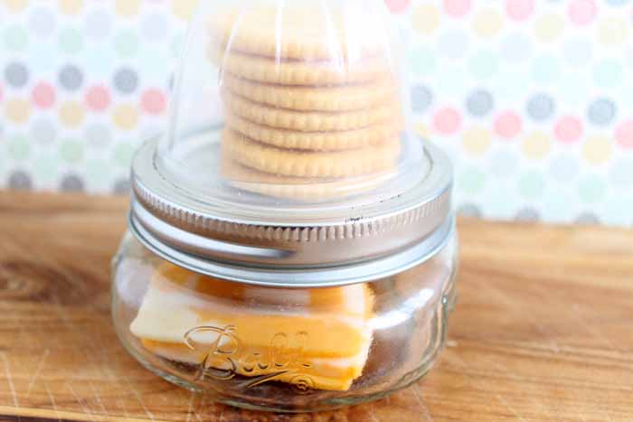 mason jar with cheese and meat inside and crackers on top 
