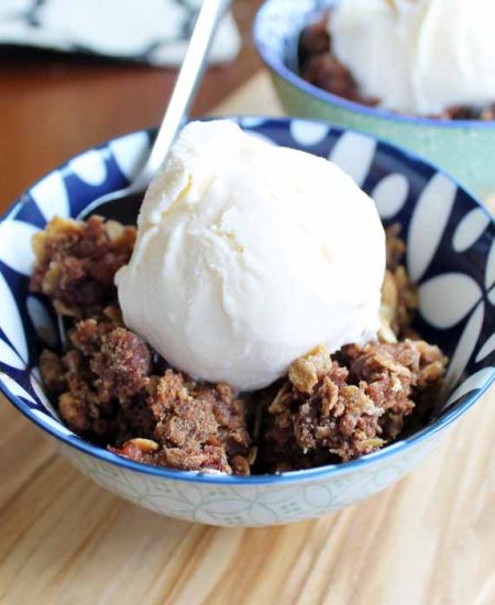 A bowl of apple crisp with vanilla ice cream and spoon on wood