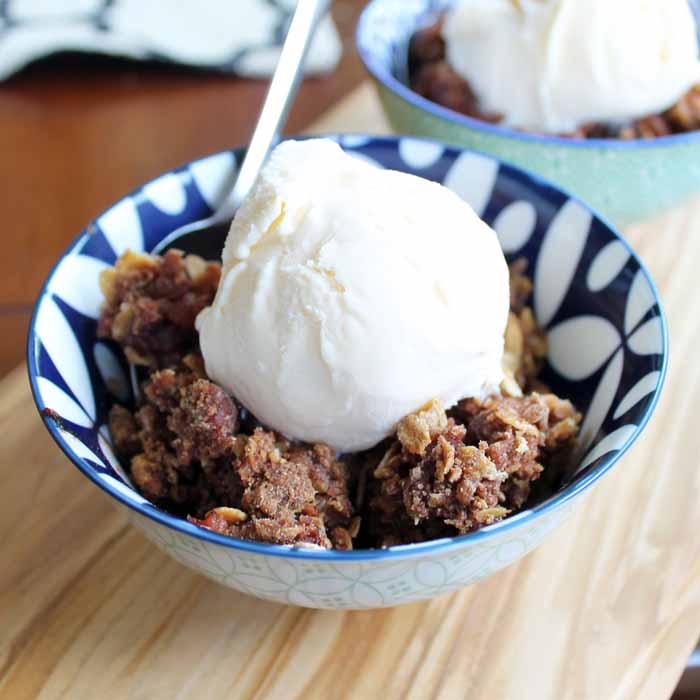 A bowl of apple crisp with vanilla ice cream and spoon on wood