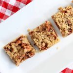 three pieces of apple bars on a white plate with a red checkered tablecloth