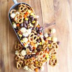 A close up halloween snack mix with a scoop on a wooden table
