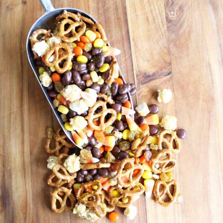 A close up halloween snack mix with a scoop on a wooden table