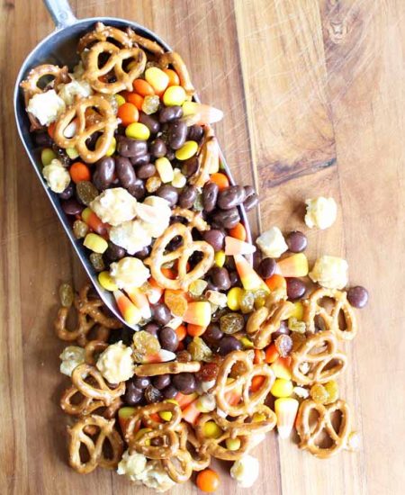 A close up halloween snack mix with a scoop on a wooden table