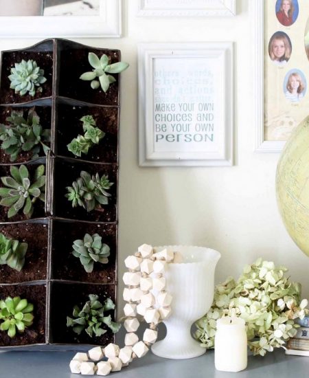 vignette of succulent garden, gallery wall, globe and wooden beads coming out of a white vase