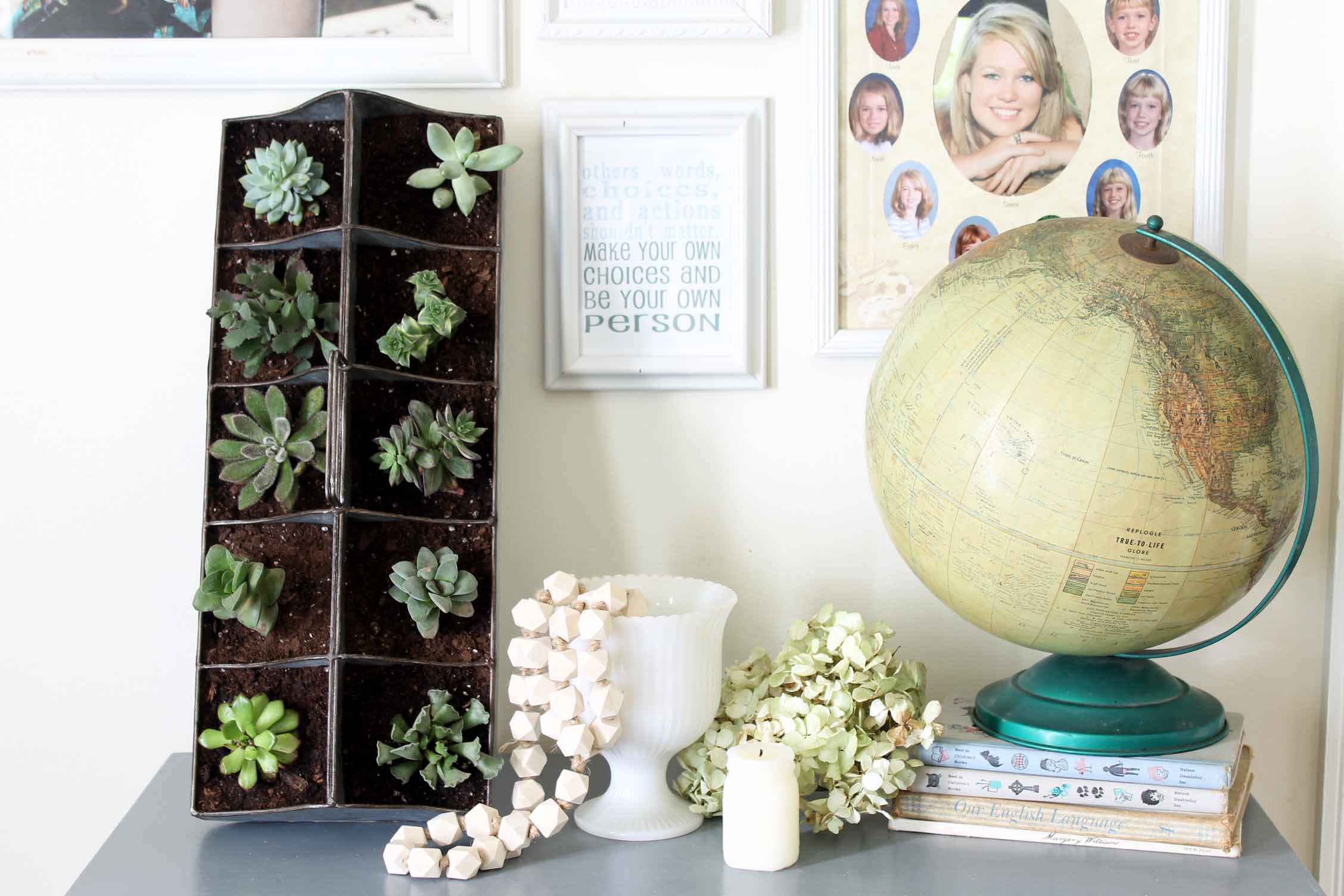 vertical succulent garden in front of a gallery wall with a globe, white vase with wooden beads