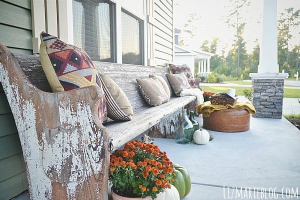 Front porch with weathered wood bench, mums and pillows