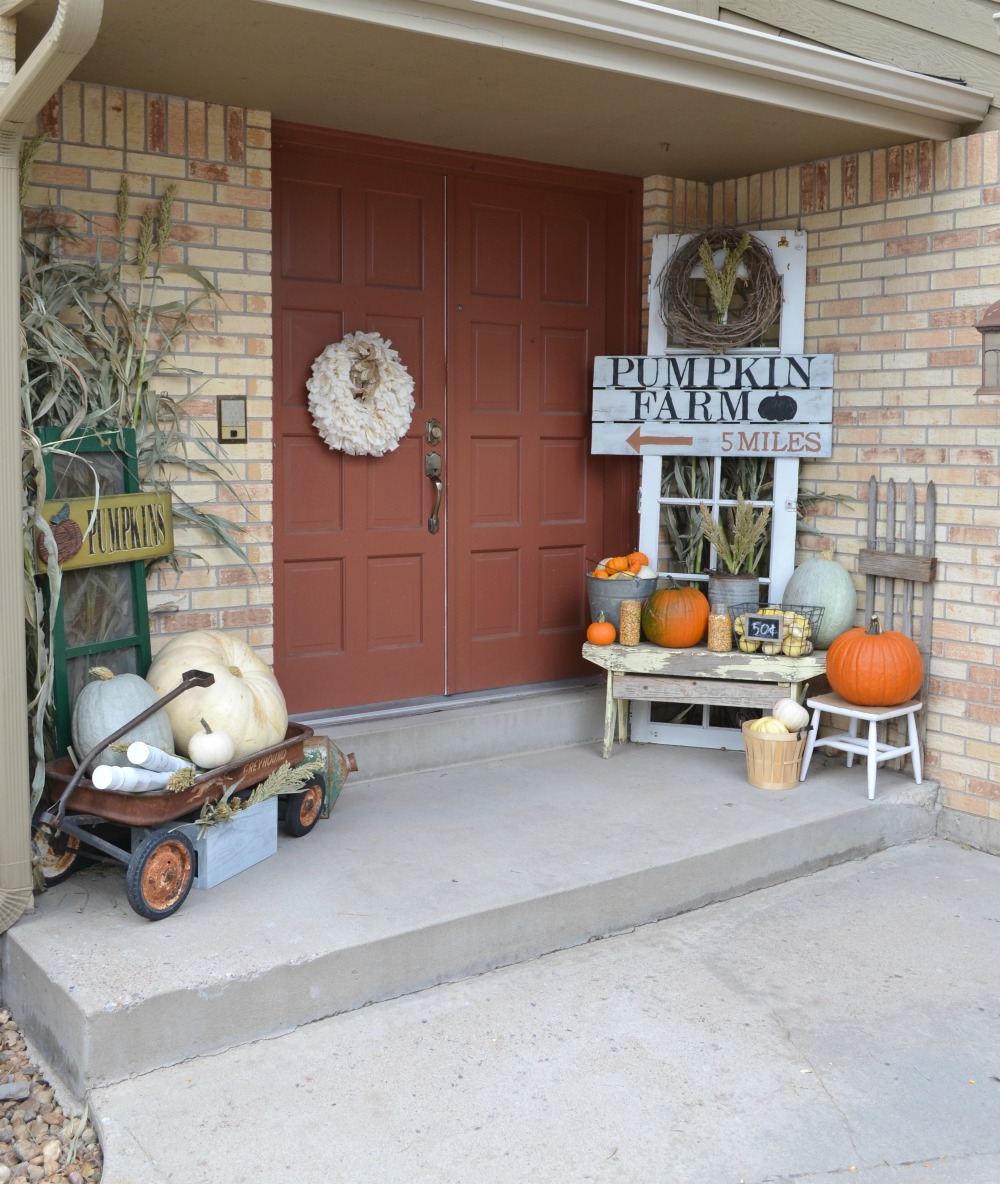 Front porch with terra cotta colored door, corn husk wreath, fall signs and pumpkins