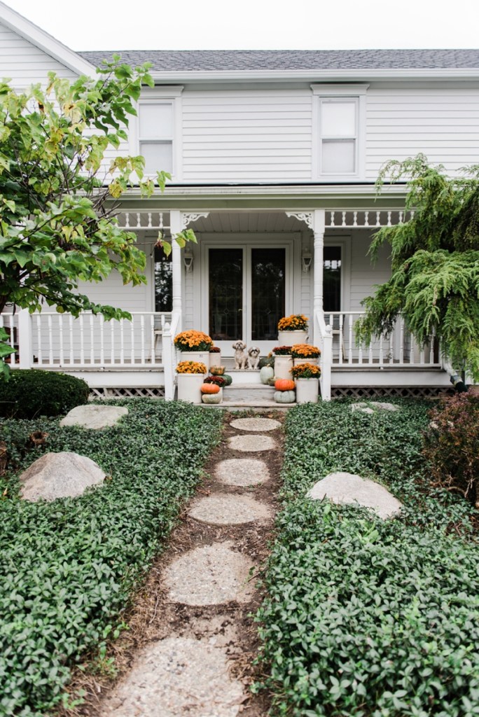 White house with fall decorated front porch. Orange mums and pumpkins