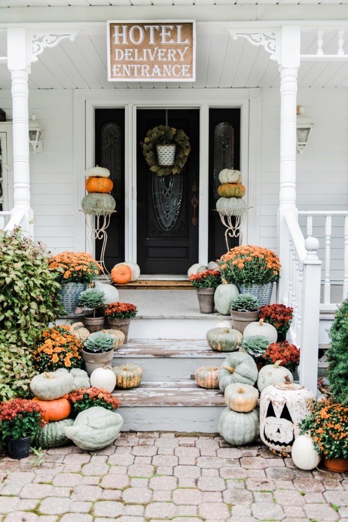 Front porch with pumpkin topiaries, mums, heirloom pumpkins and fall wreath on black front door