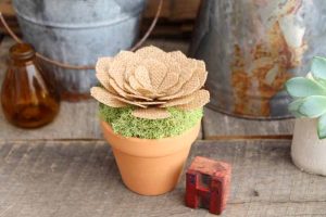 A close up of a terra cotta pot with burlap flower in a rustic wood setting