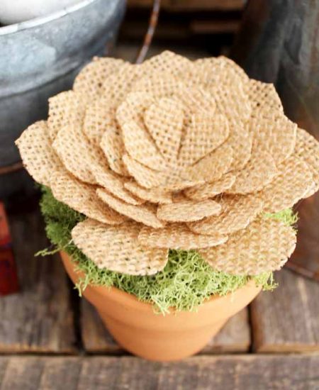 close up shot of a burlap flower in a small pot on a weathered wood backdrop