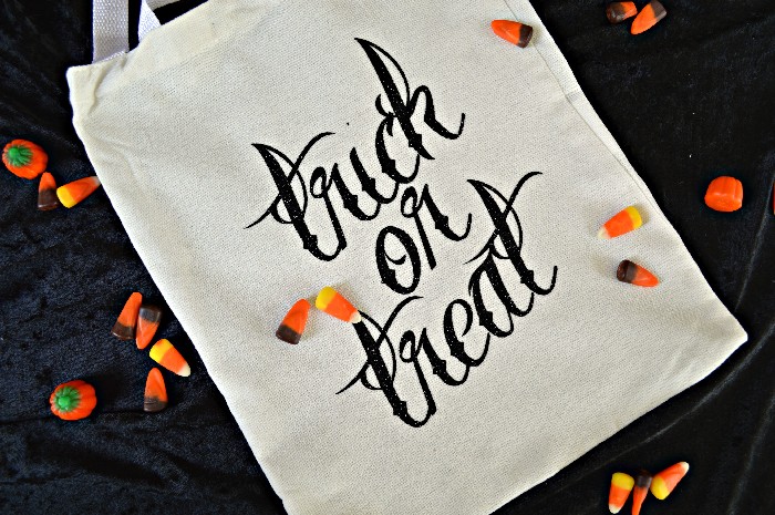 white trick or treat tote bag on black backdrop with candy corn sprinkled on top