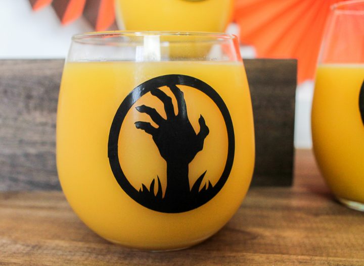 A close up of a glass of orange drink with a Halloween silhouette