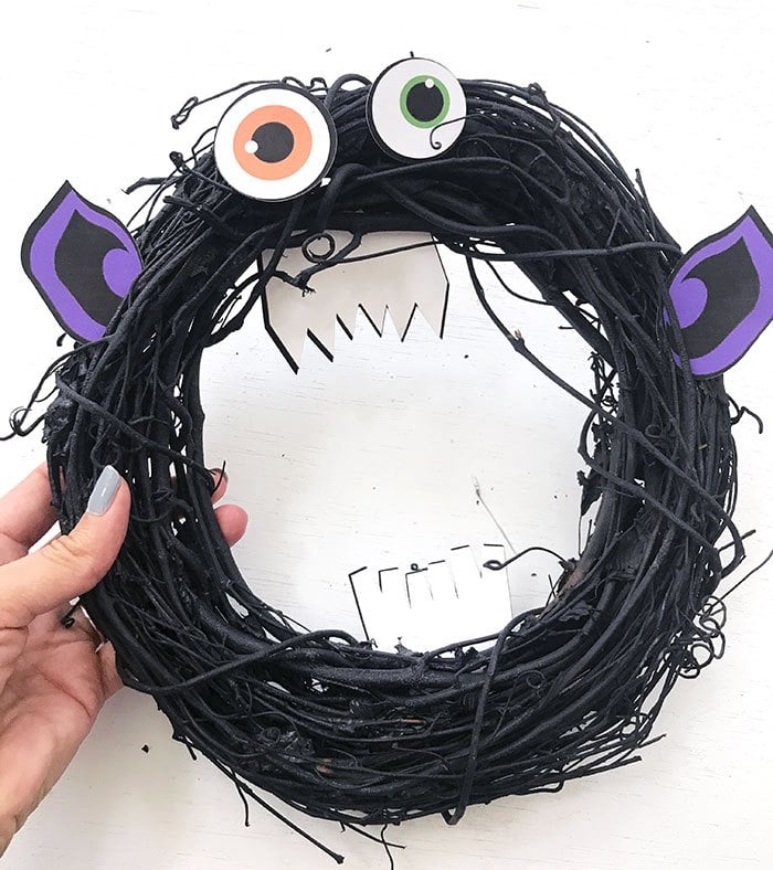 black grapevine wreath with google eyes and purple monster ears on white backdrop