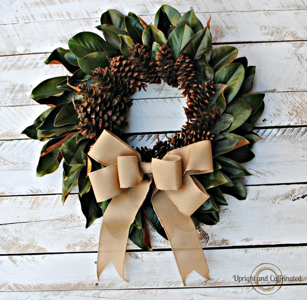 magnolia wreath with pine cones and burlap bow on white wood backdrop