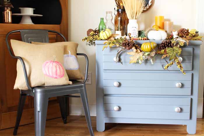 Blue dresser with burlap pillows in galvanized chair with fall display