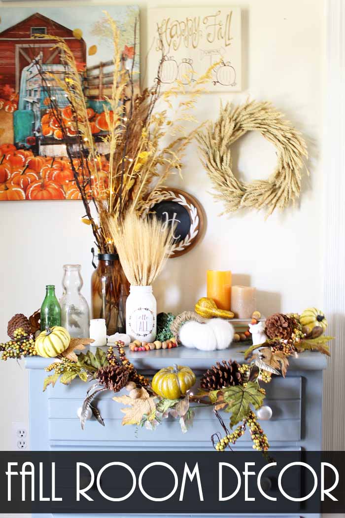 fall display on a blue dresser with a wheat wreath, pumpkins and a wreath with pumpkin garland