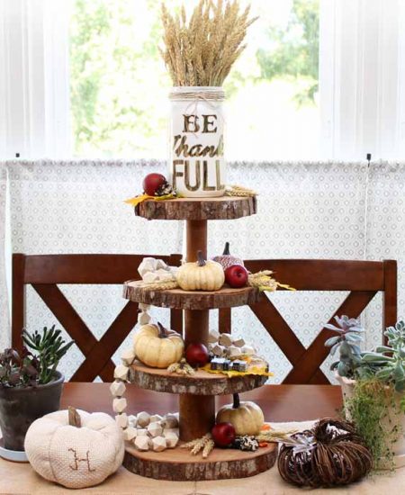 A tiered wood server with fall accessories in front of a window