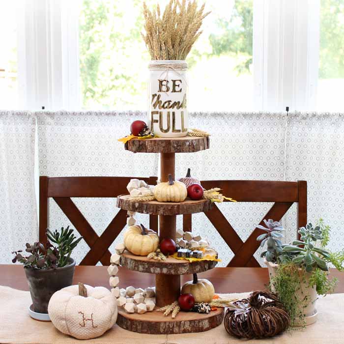 A tiered wood server with fall accessories in front of a window