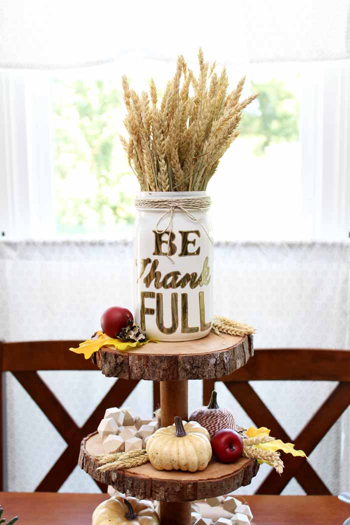 A vase that says be thank full with wheat on a table