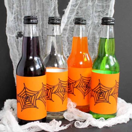different colors of glass drinks with orange Halloween labels on spider web backdrop